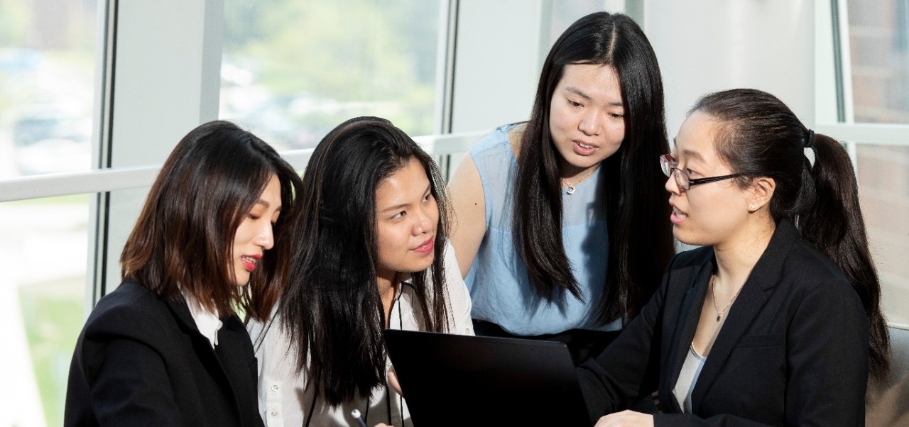 Four Asian School of Management students talking with each other behind a laptop computer. 