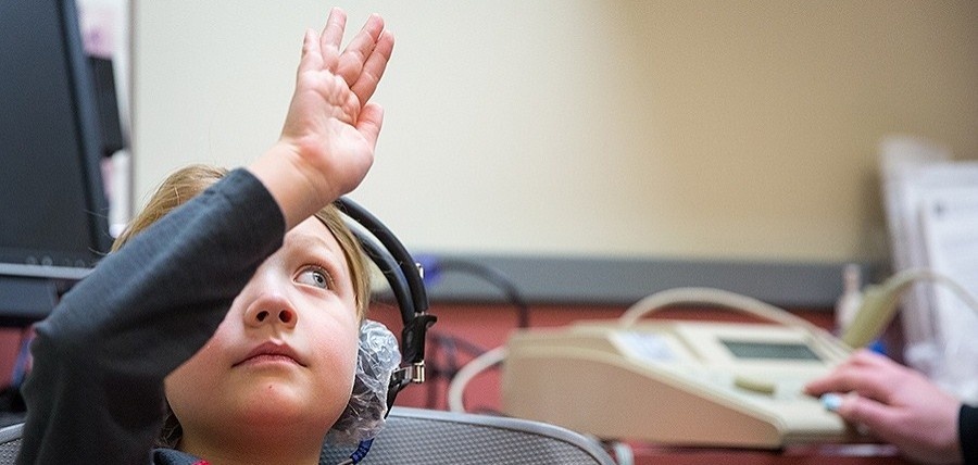 Young student in an audiology clinic raising their right hand. 