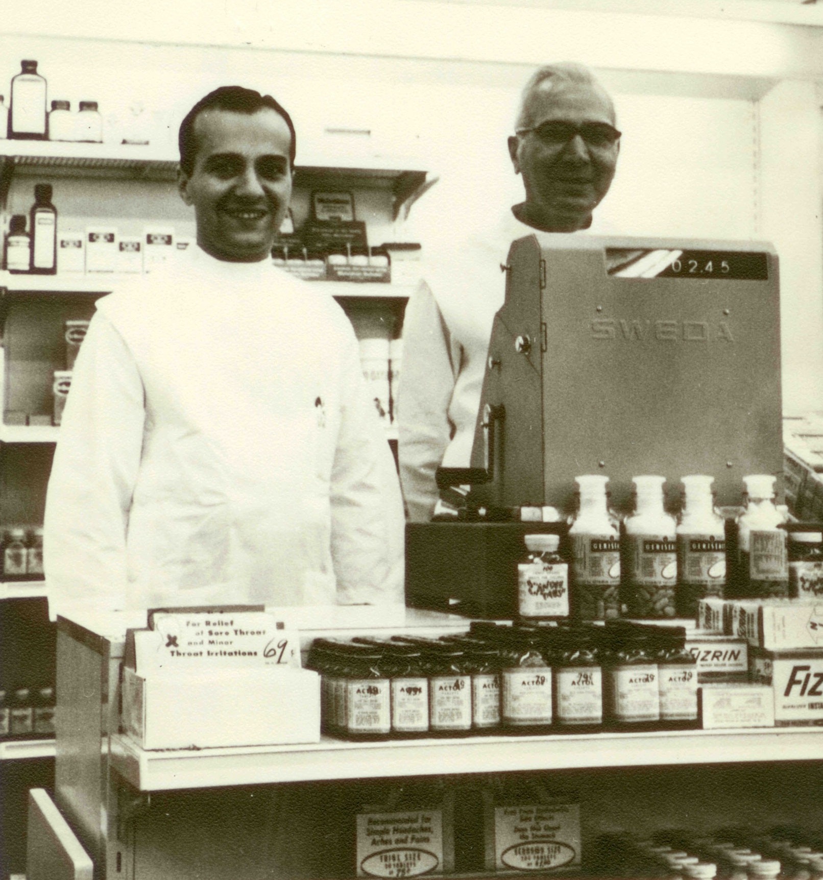 Zoom image: Henry Panasci Jr., and his father, Henry Panasci Sr., behind the counter at the first Fay's Drug Store in Syracuse, New York, in 1958. 